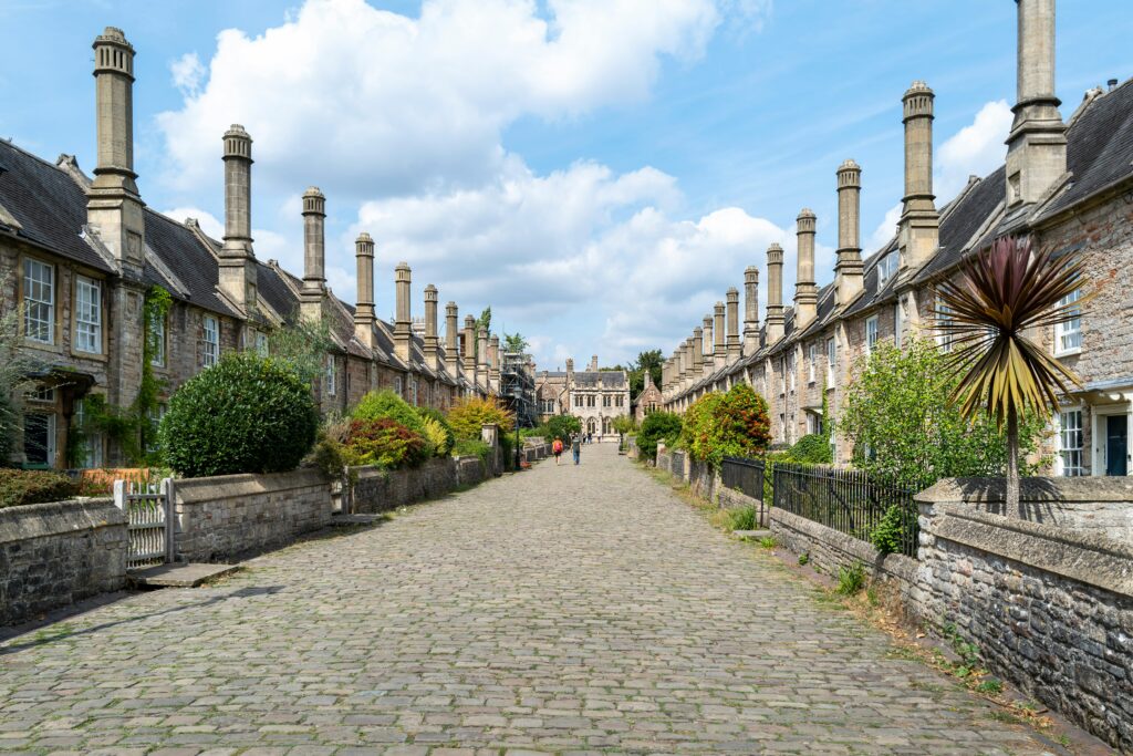 Picturesque medieval street in Wells, England featuring historic chimneys against a blue sky.